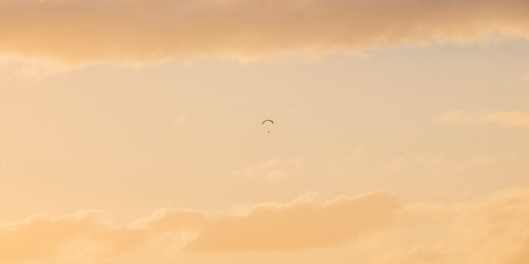 Paraglider floating through golden blue sunset or sunrise sky over Camps Bay, Cape Town.