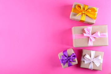 Simple composition with multiple presents wrapped in hand made blank craft paper gift wrap, pastel satin bow. Simple giftbox, wrapping, giftwrap, silk ribbon. Pink background, close up, copy space.