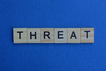 The word threat from brown wooden letters lies on a blue table