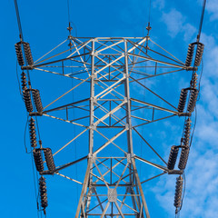 High towers of a high voltage power line against a blue sky, bottom view