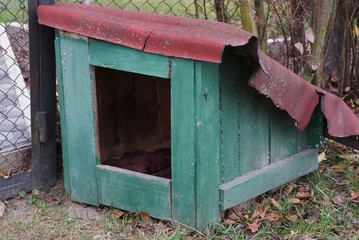 empty green doghouse from wooden boards on the street near the fence