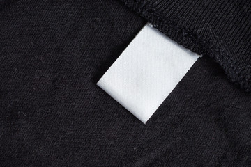 Blank white laundry care clothing label on black fabric texture