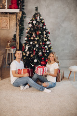 Obraz na płótnie Canvas Unrecognizable couple in t-shirts and jeans sorting beautiful gifts for their family under the Christmas tree in decorated living room. They are sitting on the floor and putting presents under the