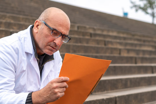 Absorbed Medical Doctor Or Dentist Sitting On Outdoor Stairs And Reading A Clinical Study Report