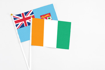 Cote D'Ivoire and Fiji stick flags on white background. High quality fabric, miniature national flag. Peaceful global concept.White floor for copy space.