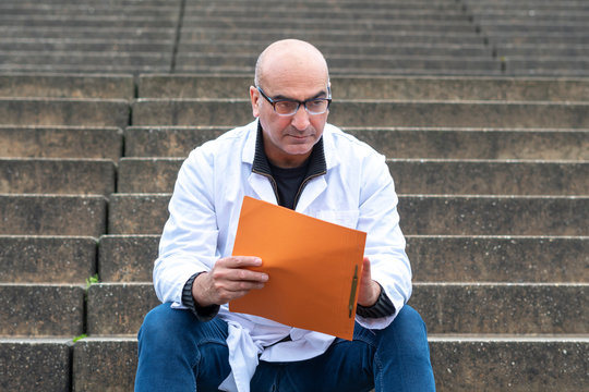 Absorbed Medical Doctor Or Dentist Sitting On Outdoor Stairs And Reading A Clinical Study Report