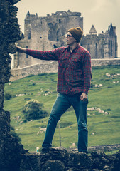 Young man exploring epic ruins with castle on the hill in background