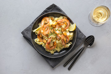 Pasta reginelle with seafood, shrimps, mussels black plate on gray stone table, Top view. Traditional dish in Italian restaurant.