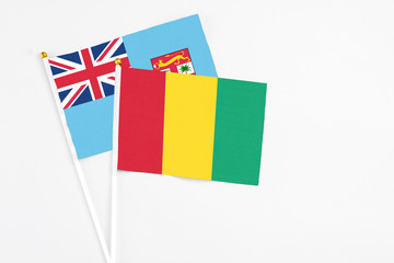 Guinea and Fiji stick flags on white background. High quality fabric, miniature national flag. Peaceful global concept.White floor for copy space.
