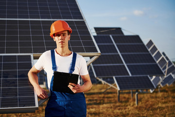 Male worker in blue uniform outdoors with solar batteries at sunny day