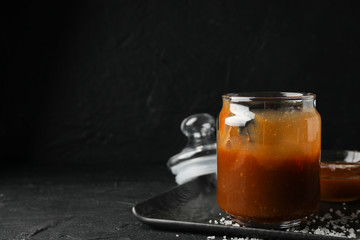 Glass jars with salted caramel on black background, space for text