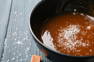 Bowl with salted caramel and candies on wooden background, close up