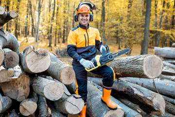 Portrait of a cheerful professional lumberjack in protective workwear standing with a chainsaw on a...