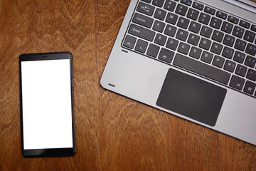 Smartphone with white screen and laptop keyboard on wooden background