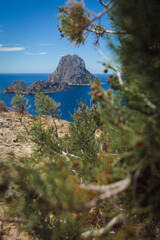 Fototapeta na wymiar View of famous mysterious island Es Vedrà from famous view point on cliffs above beach Cala D'Hort beautiful island of Ibiza, Spain, scenic blue sea, horizon sky, plants and cliff rocks in foreground