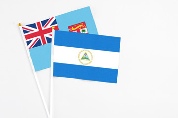 Nicaragua and Fiji stick flags on white background. High quality fabric, miniature national flag. Peaceful global concept.White floor for copy space.