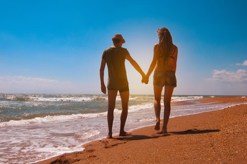 Young man and woman walk on a sandy beach near the sea at sunset