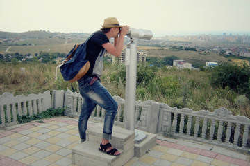 A male traveler is looking through binoculars at an observation deck. Tourism concept