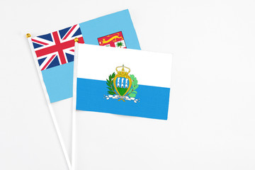 San Marino and Fiji stick flags on white background. High quality fabric, miniature national flag. Peaceful global concept.White floor for copy space.