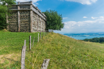 This fortified town, called oppidum, dates from the Celtic period, around 124 a. C. Construction of wood on a slope of green grass, some tree and a lake in the background with the blue sky with some c