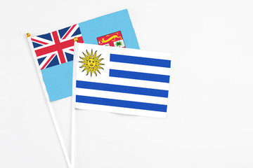 Uruguay and Fiji stick flags on white background. High quality fabric, miniature national flag. Peaceful global concept.White floor for copy space.