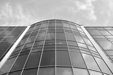 Curtain wall made of toned glass and steel constructions under sky. A fragment of a building. Black and white.