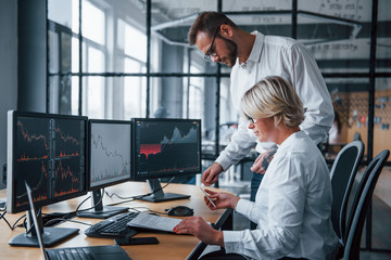 Analyzing information together. Two stockbrokers in formal clothes works in the office with financial market