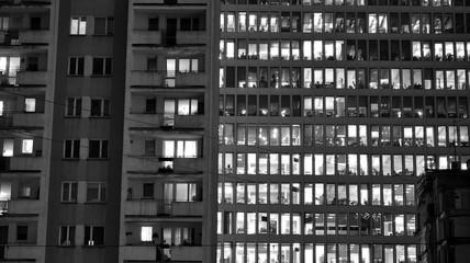 Pattern of office buildings windows illuminated at night adjacent to an old residential building. Lighting with Glass architecture facade design with reflection in urban city. Black and white.
