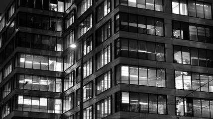 Obraz premium Pattern of office buildings windows illuminated at night. Lighting with Glass architecture facade design with reflection in urban city. Black and white.