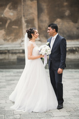 Gorgeous happy couple standing close to each other and looking in eyes at old city background, wedding photo, European city, wedding day in Lviv