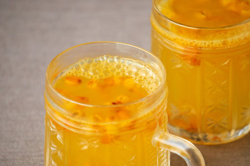 Sea buckthorn tea in glass mugs on brown background 