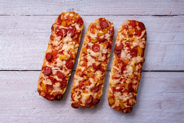 Pizza baguettes with salami and white wooden background