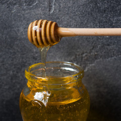 A jar of liquid honey from Linden flowers and a stick with honey on a dark background.