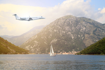 White private jet business jet flies against backdrop of beautiful spectacular views of boat in middle of bay with  mountain behind
