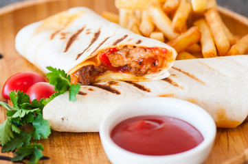 Burrito rolls and fries with ketchup on a wooden plate.