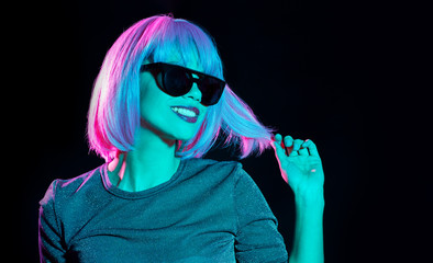 nightlife, fashion and people concept - happy young woman wearing pink wig and black sunglasses in neon ultra violet light over black background