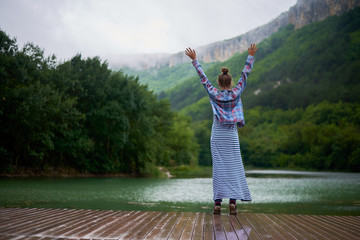 Fototapeta na wymiar Casual dressed hiking woman under the rain dancing near the lake in mountains.