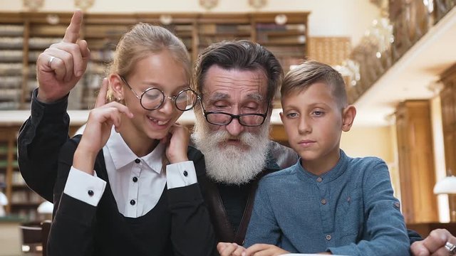 Handsome bearded old man reading book, raised finger that his teenage grandchildren understand the contant of book