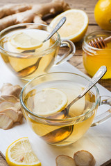 Two cups of natural herbal tea ginger lemon and honey on a wooden background.