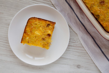 Homemade Cheesy Amish Breakfast Casserole on a white plate on a white wooden background, top view. Flat lay, overhead, from above.