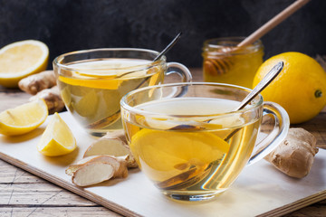 Two cups of natural herbal tea ginger lemon and honey on a wooden background.