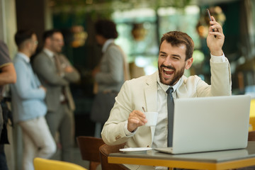 Handsome young businessman working at laptop with cup of coffee in restaurant.