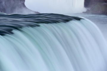 A stream of water descends from a cliff down. Niagara Falls nearby. USA.