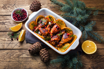 Baked chicken drumstick with oranges and cranberries in a baking sheet on a wooden background. Christmas food Table with decorations.