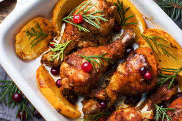 Baked chicken drumstick with oranges and cranberries in a baking sheet on a wooden background. Christmas food Table with decorations.