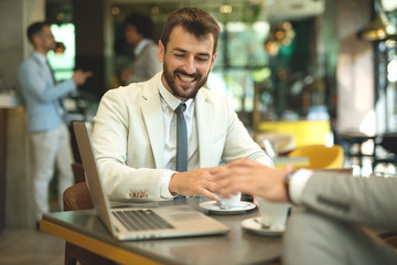 Handsome Smiling Freelancer Showing Finished Project on laptop to a Colleague in Coffee Restaurant