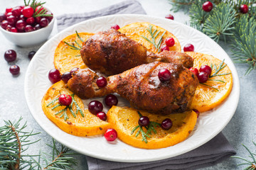 Baked chicken drumstick with oranges and cranberries in a plate light grey background. Christmas food Table with decorations.