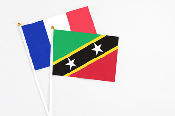 Saint Kitts And Nevis and France stick flags on white background. High quality fabric, miniature national flag. Peaceful global concept.White floor for copy space.