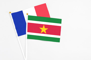 Suriname and France stick flags on white background. High quality fabric, miniature national flag. Peaceful global concept.White floor for copy space.