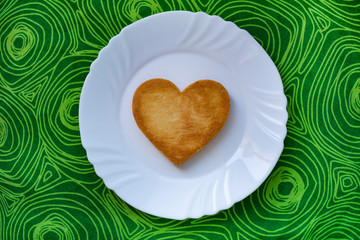 Heart-shaped cookie, on a white round plate, on green background.